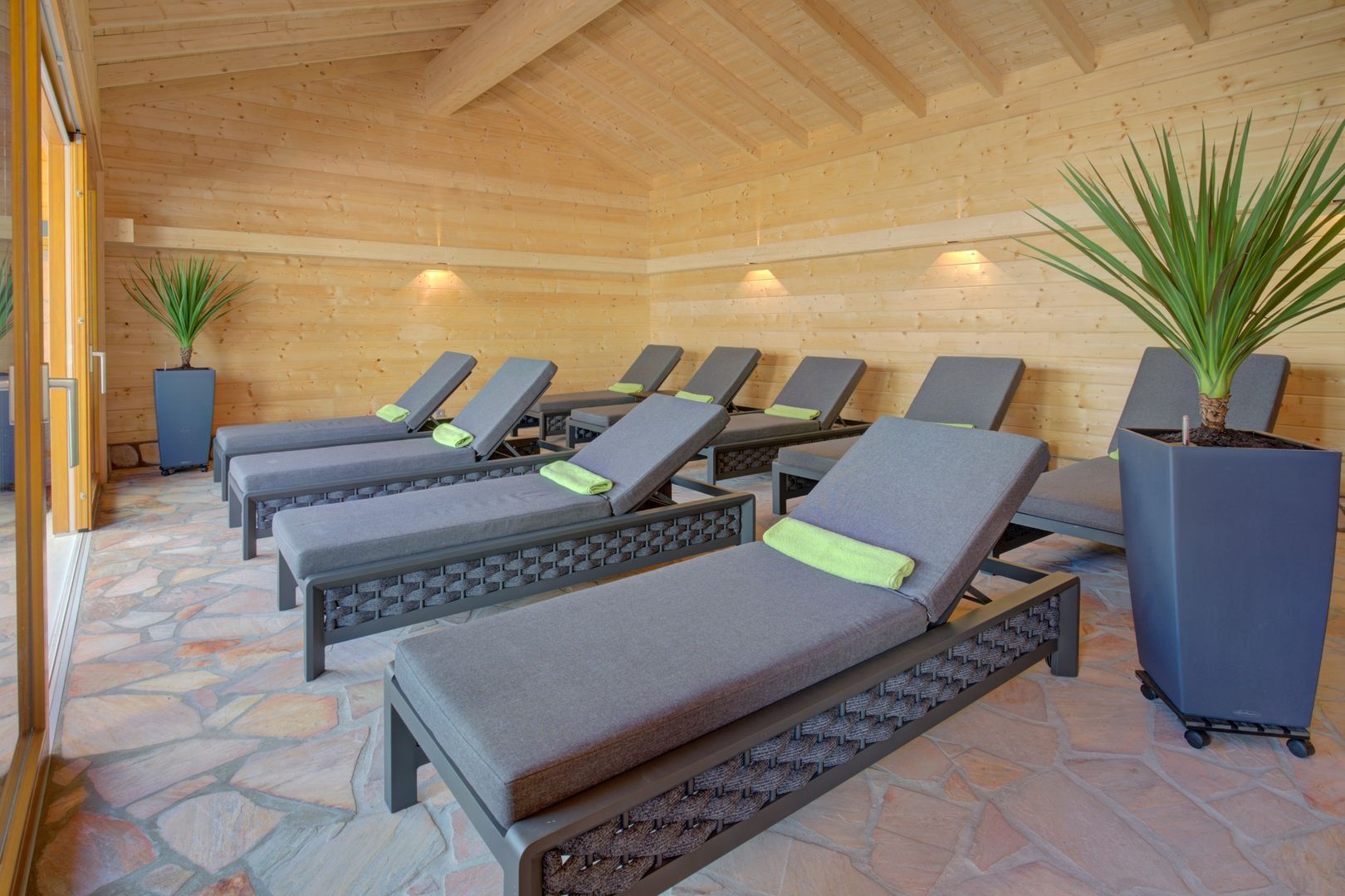 Une salle de bien-être calme avec huit fauteuils gris, chacun recouvert d'une serviette verte.