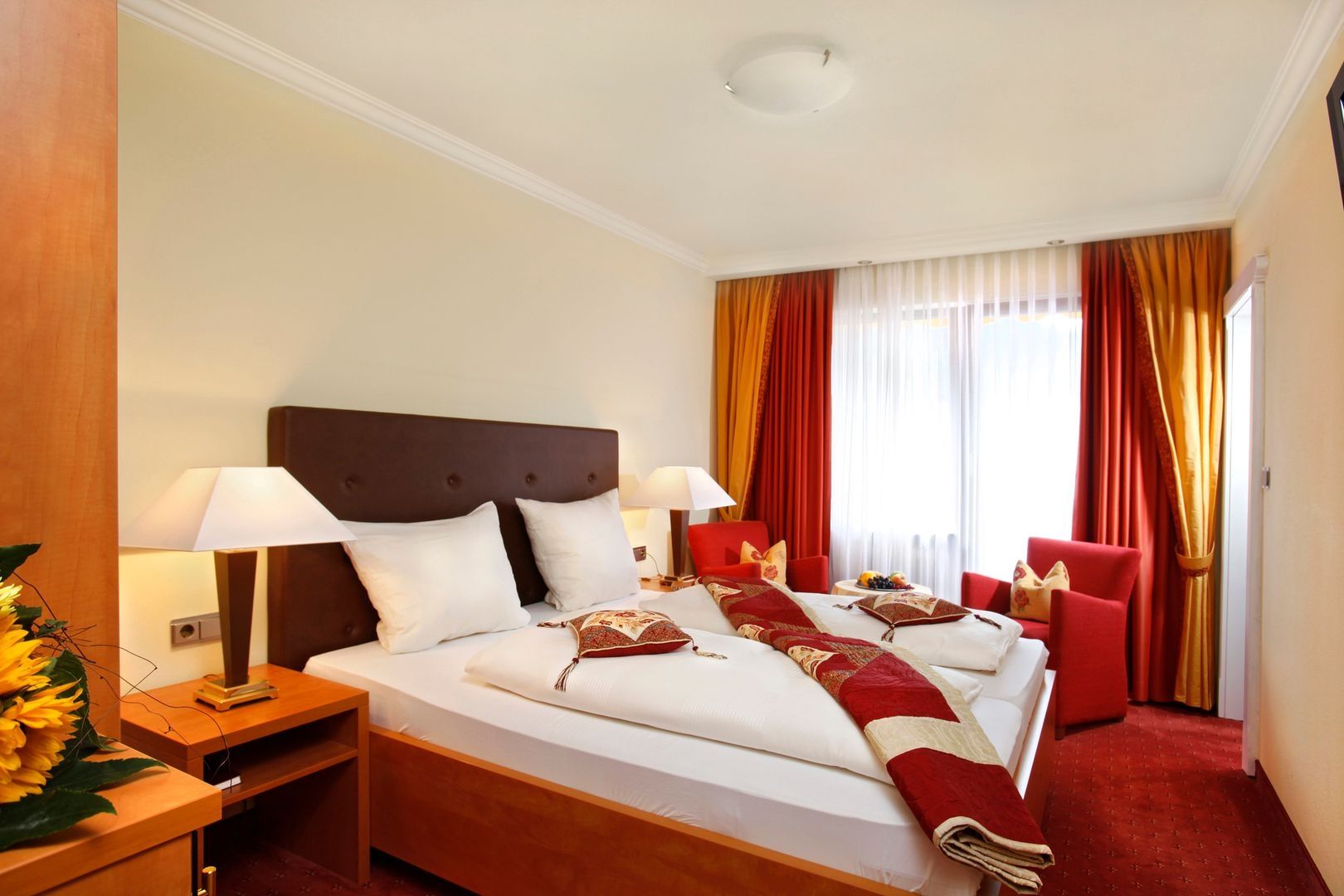 Elegant hotel room with a comfortable bed, brown headboard, white bedding, and red accents